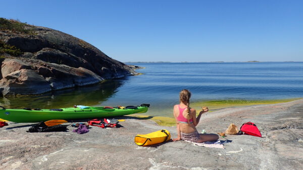 En flicka njuter av en kopp te på stranden med en kajak vid sin sida en vacker sommardag i Skärgårdshavet.
