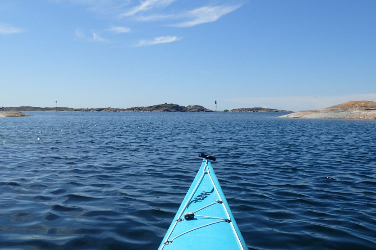 Spetsen på en ljusblå kajak och ett par små öar vid horisonten.